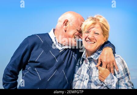 Happy senior couple in love during retirement - Joyful elderly lifestyle with man whispering and smiling with her wife Stock Photo