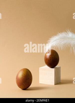 Minimalistic Easter background. A brown chicken egg stands on a beige background, an egg and a feather are out of focus in the background. Copy space Stock Photo