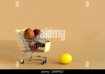 Easter eggs in a grocery cart on a beige background. A yellow egg lies separately. Easter background concept with copy space Stock Photo