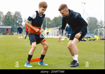 Soccer Coach With Young Player. Boy on Football Field Stretching on Exercise Mat. Male Coach and Personal Trainer Giving Advices to Young Athlete Stock Photo
