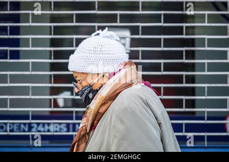 London, UK - 5 February, 2021 - a senior woman wearing a protective face mask passing by a closed shop on Wood Green high street Stock Photo