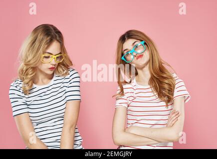 two cheerful girlfriends in striped t-shirts are standing side by side on a pink background Stock Photo