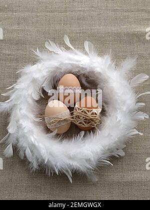Easter composition decorated by lace Easter eggs in white feather wreath on linen background Stock Photo