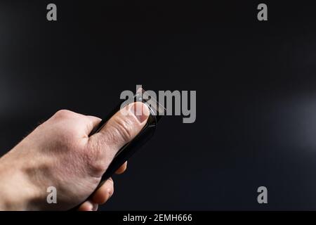 Man's hand holding electric trimmer for shaving, on black background with copy space. Stock Photo