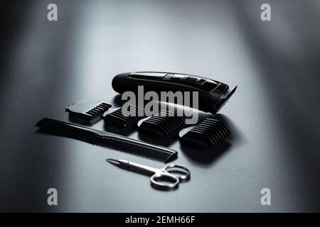 Electric trimmer with other barber tools on black background with light on it. Stock Photo