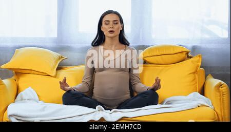 Pregnant woman meditating on couch at home Stock Photo