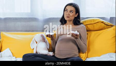 Pensive pregnant woman holding baby booties near soft toy Stock Photo