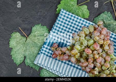A bunch of red grapes with leaves and blue tablecloth on dark background Stock Photo