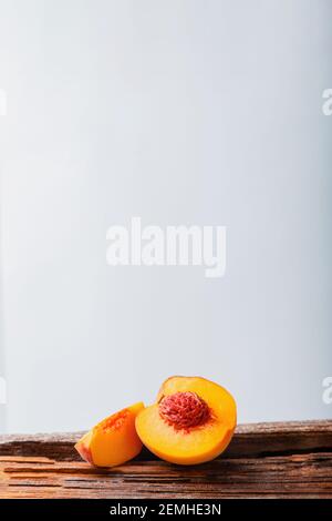 Peaches with leaves on wooden board. Peach in halves with bone. Ripe juicy peaches. Fresh organic peaches fruit on white background. Rustic minimalist Stock Photo