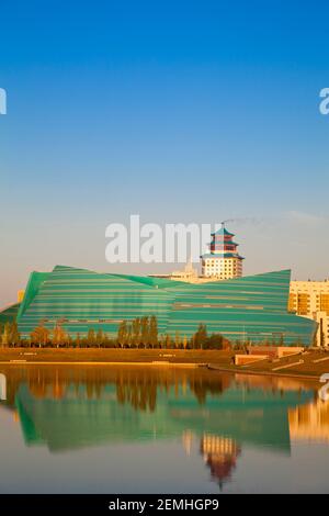 Kazakhstan, Astana, City skyline reflecting in Isahim River, looking towards the Central Concert Hall and The Beijing Palace Soluxe Hotel Stock Photo