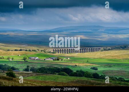 Scenic countryside view (Northern locomotive crossing Ribblehead Viaduct, hilly uplands, valley & hills, dramatic sky) - Yorkshire Dales, England UK.