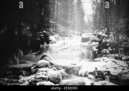 Moody long exposure shot of cascades in the small river Jaran in Bispgarden, Sweden. Light beams are coming from above. Stock Photo