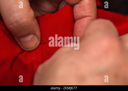 sanior old man or woman Sews with a needle and thread at home. Fingers hands of the seamstress is using a needle and red thread to sew cloth close-up Stock Photo