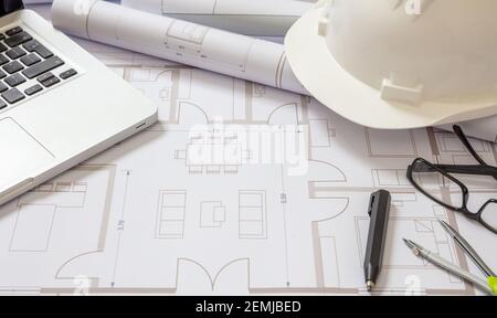 Project blueprints laptop and engineer hardhat white color on drawings background. Housing project construction, architect site office concept. Stock Photo
