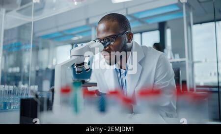 Modern Medical Research Laboratory: Portrait of Male Scientist Looking Under Microscope, Analysing Samples. Advanced Scientific Lab for Medicine Stock Photo