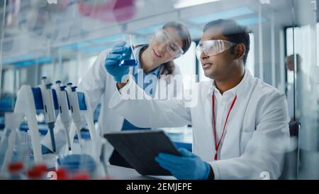 Modern Medical Research Laboratory: Two Scientists Working Together Analysing Chemicals in Laboratory Flask, Discussing Problem. Advanced Scientific Stock Photo