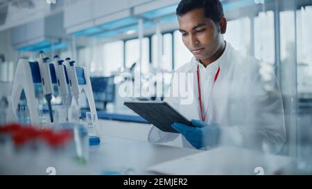 Medical Research Laboratory: Portrait of a Handsome Male Scientist Using Digital Tablet Computer to Analyse Data. Advanced Scientific Lab for Medicine Stock Photo