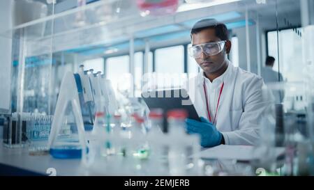 Medical Research Laboratory: Portrait of a Handsome Male Scientist Using Digital Tablet Computer to Analyse Data. Advanced Scientific Lab for Medicine Stock Photo