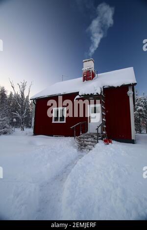 Small snowbound house in northern Sweden with smoking chimney. Stock Photo