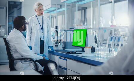 Modern Medical Research Laboratory: Two Scientists Use Computer with Green Chroma Key Screen, Specialists Discuss Innovative Technology. Advanced Stock Photo