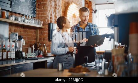 Two Diverse Entrepreneurs Have a Team Meeting in Their Stylish Coffee Shop. Barista and Cafe Owner Discuss Work Schedule and Menu on Laptop Computer Stock Photo