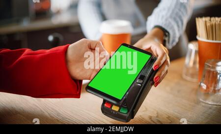Close Up of a Feminine Hand Holding a Smartphone with Green Screen Template with an NFC Payment Technology Used for Paying for Take Away Coffee in a Stock Photo