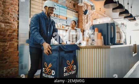 Beautiful Happy Latin Barista Serves Order of a Food Delivery Courier. Delivery Guy Puts Food in His Hot Thermal Insulated Bag and Closes it. Sunny Stock Photo