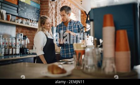 Two Diverse Entrepreneurs Have a Team Meeting in Their Stylish Coffee Shop. Barista and Cafe Owner Discuss Work Schedule and Menu on Tablet Computer Stock Photo