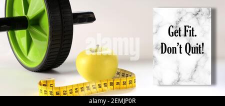 Healthy lifestyle motivational quote. Diet fitness and Healthy life Concept. Motivational Quote text Get Fit. Don't Quit. Apple, measure tape, sport home gym equipment ab roller for diet slimming Stock Photo