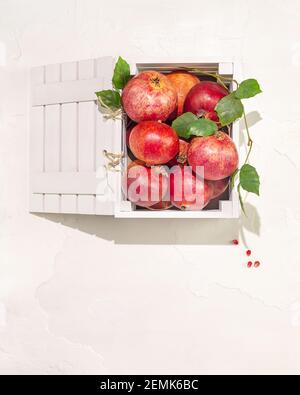 Fresh, ripe pomegranates with leaves in a wooden box on a white background. Healthy season foods with lots of vitamins. Eco friendly fruits packaging Stock Photo