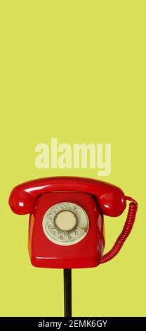 red landline rotary dial telephone on the top of a black tubular stand, on a yellow background, with some blank space on top, in a vertical format to Stock Photo