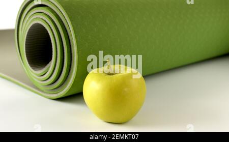 Yoga fitness, health life style. Yoga rolled green mat and green apple on white background. Place for text. Healthy lifestyle, fitness, sport concept Stock Photo