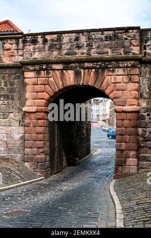 A narrow road passes under an attractive red sandstone arched bridge built into the grey stone blocks of the ancient quay walls in Berwick upon Tweed Stock Photo
