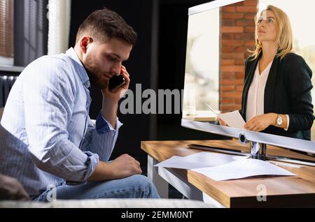 Working process. Financial manager is talking on phone, reporting on network monitor to his female boss. Young businessman working on start up project Stock Photo