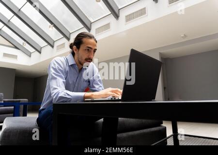 latin male professional using a laptop, very concentrated doing freelance work in the office. talking by video call. Stock Photo