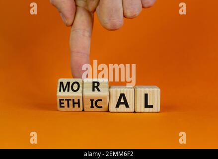 Ethical or moral symbol. Businessman turns wooden cubes and changes the word 'moral' to 'ethical' on a beautiful orange table, orange background. Busi Stock Photo
