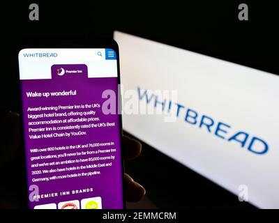 Person holding mobile phone with web page of British hospitality company Whitbread plc on screen in front of logo. Focus on center of phone display. Stock Photo