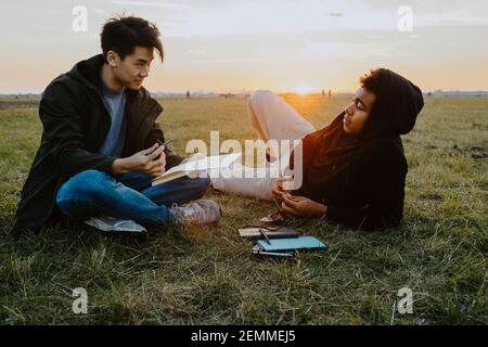 Male friends sitting in park during sunset Stock Photo