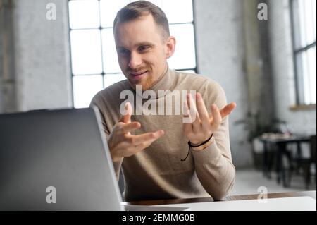 Young handsome businessman entrepreneur sitting at the desk looking at laptop, positive hipster man with the beard pitching the project idea to client or management team online on a video call Stock Photo