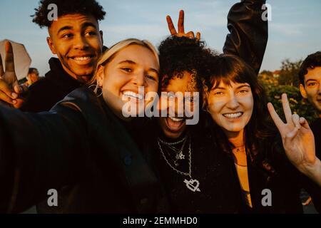 Portrait of cheerful friends taking selfie outdoors during sunset Stock Photo