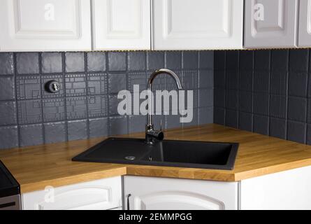 Close up view of new modern kitchen solid wood oak counter with built in black rectangular granite sink, repainted gray color tile wall. Corner. Stock Photo
