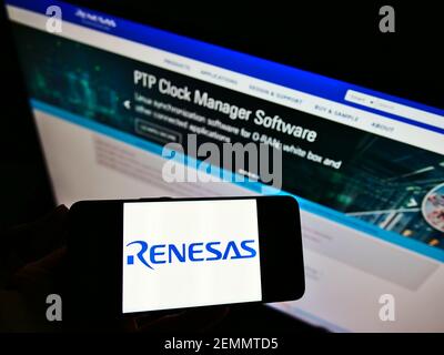 Person holding smartphone with logo of Japanese company Renesas Electronics Corporation on screen in front of website. Focus on phone display. Stock Photo