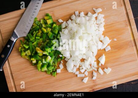 Chopped Green Bell Pepper and Onion on a Bamboo Cutting Board: Overhead view of diced vegetables on a wooden chopping board Stock Photo