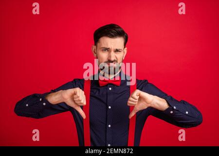 Photo of young unhappy upset sad gentleman showing thumb-up disapproval isolated on red color background Stock Photo