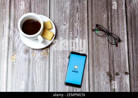 A mobile phone or cell phone on a wooden table with the Waze Maps app open next to a coffee and glasses Stock Photo