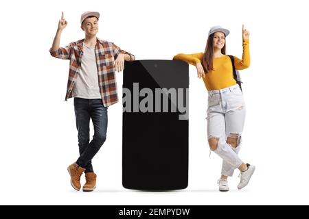 Young male and female leaning on a big mobile phone and pointing up isolated on white background Stock Photo