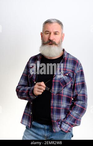 Studio portrait of confident mature bearded man in casual clothes looking at camera, eyeglasses in hands, white background Stock Photo
