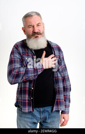 Mature caucasian man dressed in casual clothes feels bad, holding hand on chest having heart pain, white background Stock Photo