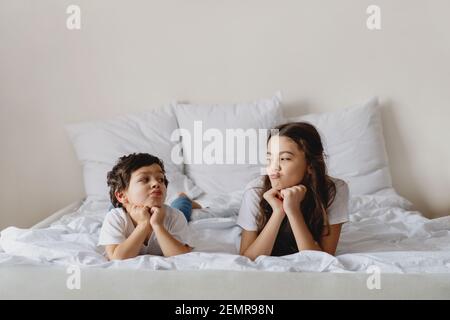 Cute little boy and his sister looking at each other while lying on a bed. Stock Photo
