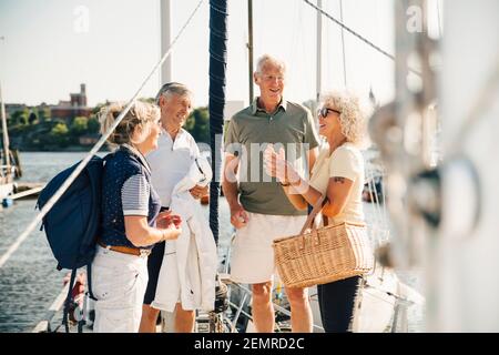 Male and female senior friends talking with each other while standing in boat on sunny day Stock Photo